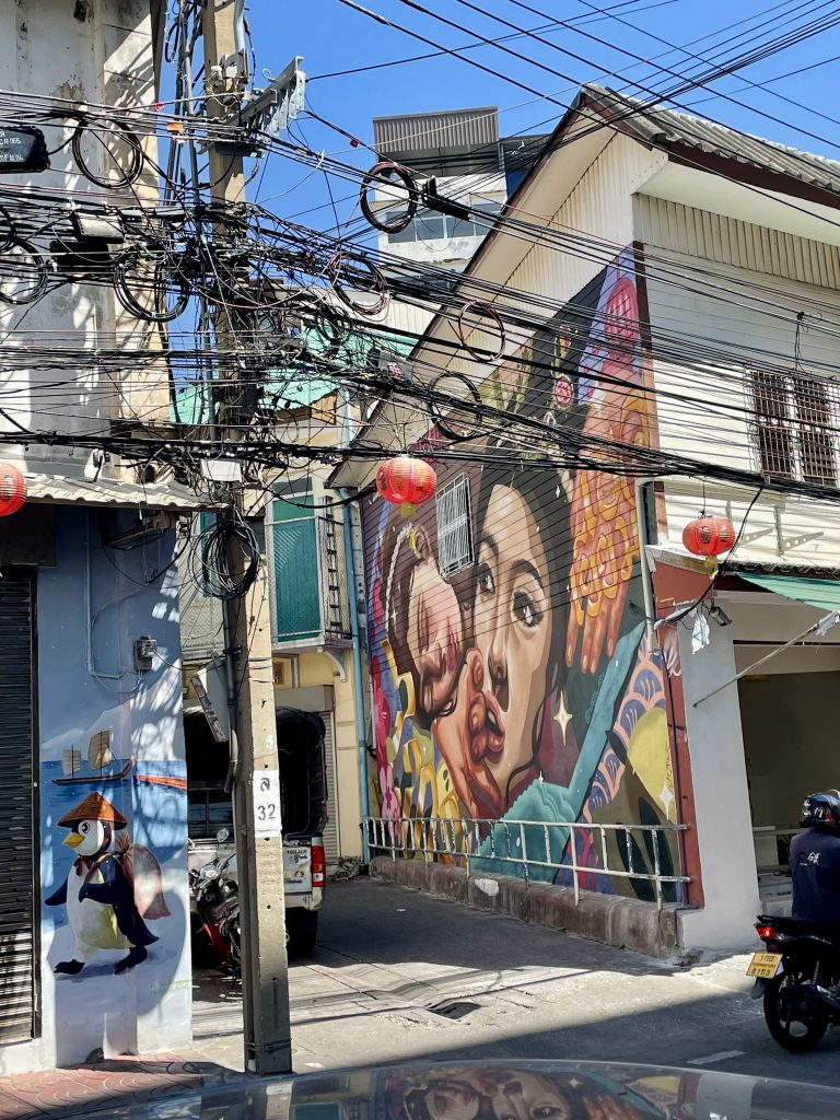 Song Wat Road ein Graffiti an der Wand mit einem Frauenkopf darauf. Wildes Kabelgewirr ist davor