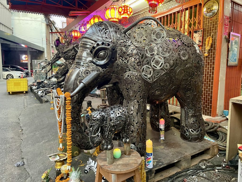 Im Vordergrund esteht ein rieser Elefant der aus Metalschrott gebaut wurde.