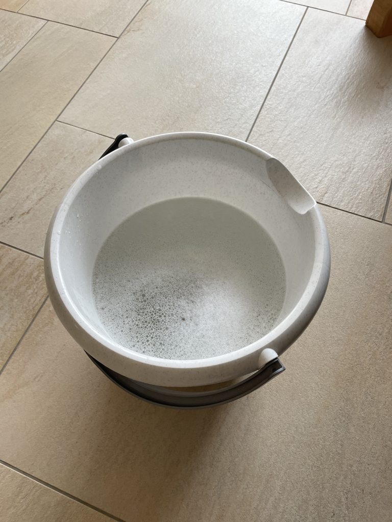 Ein Putzeimer mit Putzwasser darin steht auf einem Fliesenboden