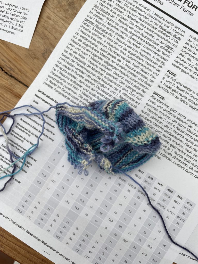 ein halb aufgetrenntes Strickstück liegt auf einer Strickanleitung auf einem Holztisch