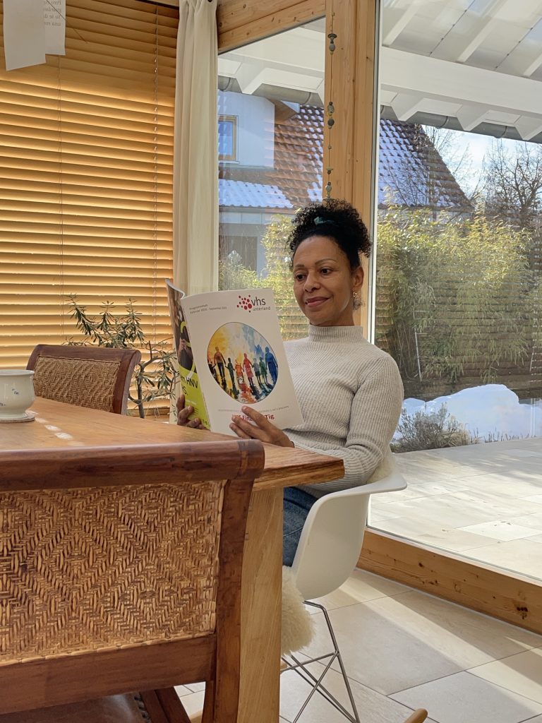 Eine Frau sitzt a einem Holztisch und ist das neue Programm der Volkshochschule