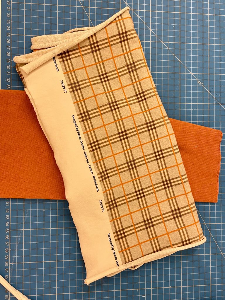 ein karierte Stoff und eine orange farbener Stoff liegen auf einer bleuen Scheidematte