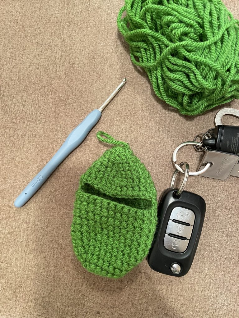 ein grüner gehäkelter Schlüsselanhänger und eine Schlüssel rechts daneben