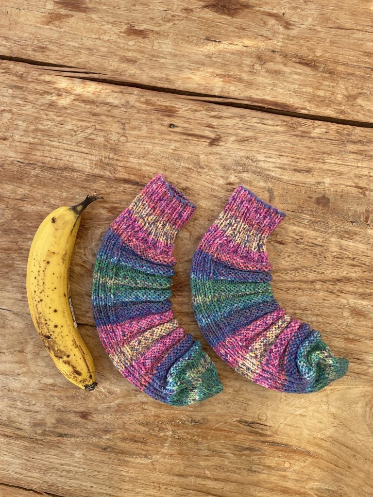 Ein paar bunte Wollesocken und daneben liegt eine Banane, da man die Form der Socken Bananensocken nennt