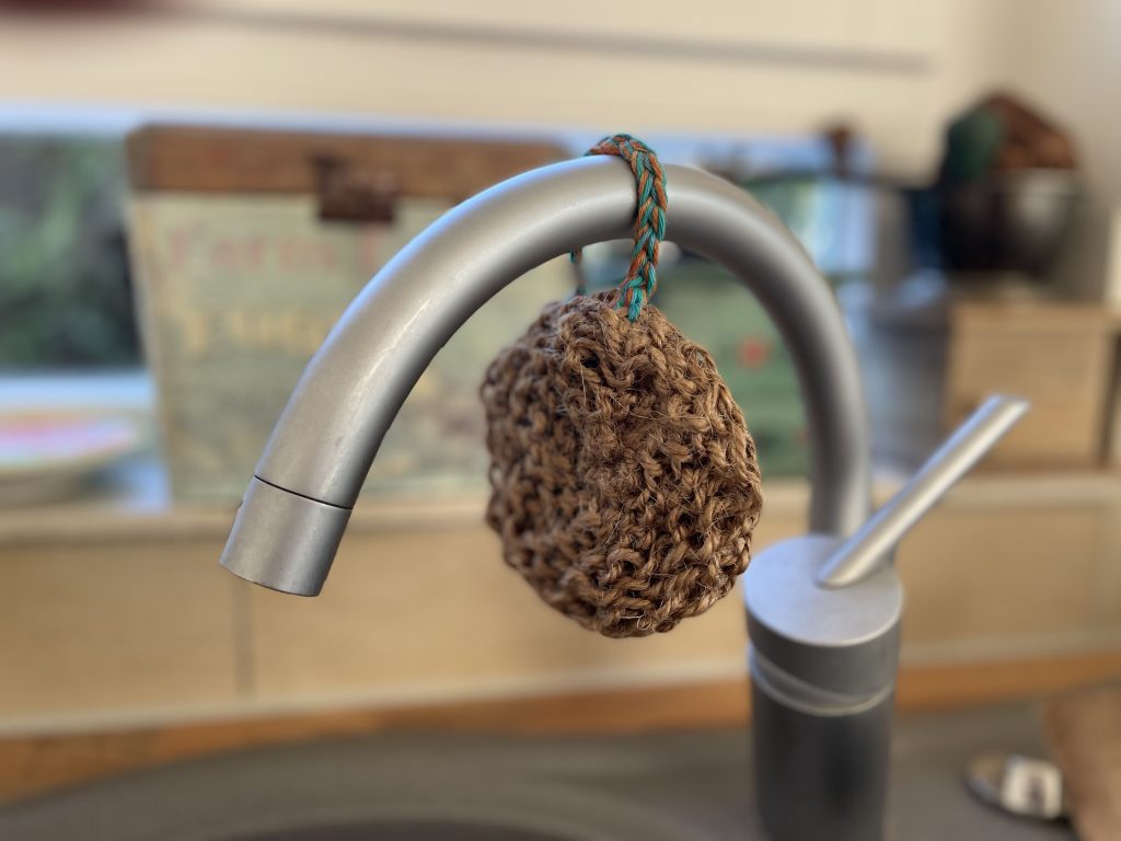 Ein No-Plastik Spülschwamm aus Paketschnur gestrickt hängt am Wasserhahn