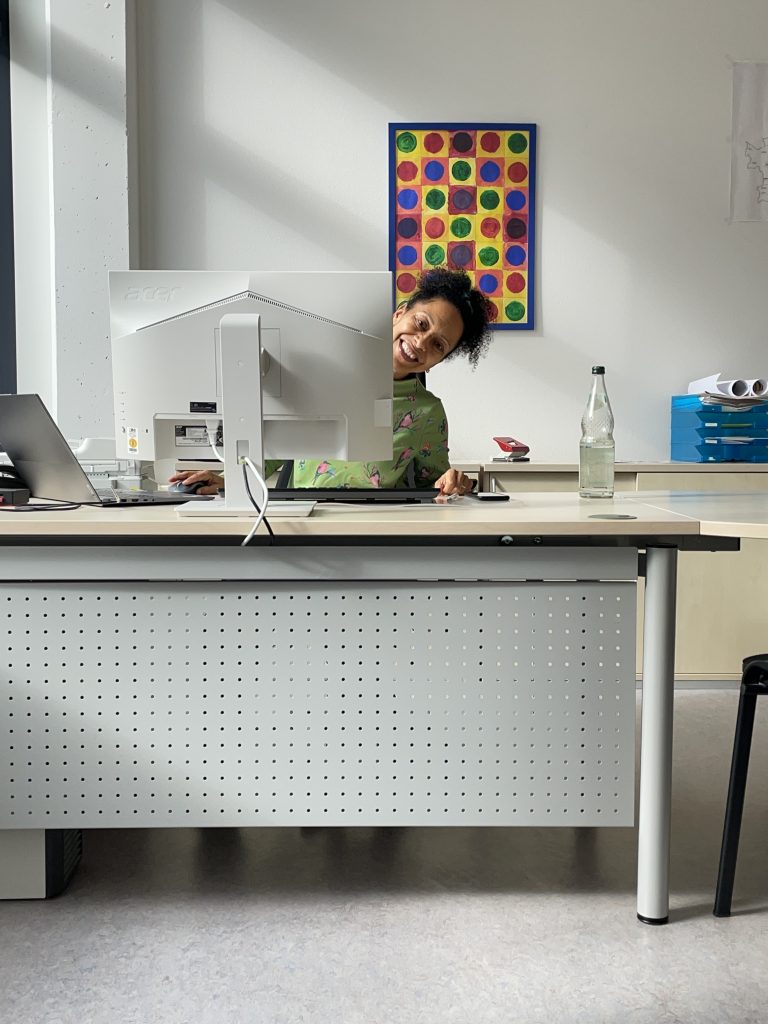 Eine Frau in einem Bro schaut hinter einem Bildschirm hervor