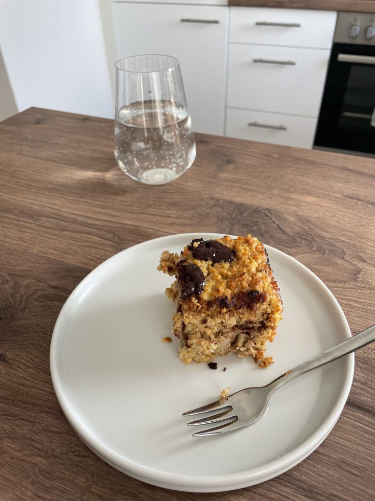 Kuchen auf einem Teller daneben steht ein Glas Wasser