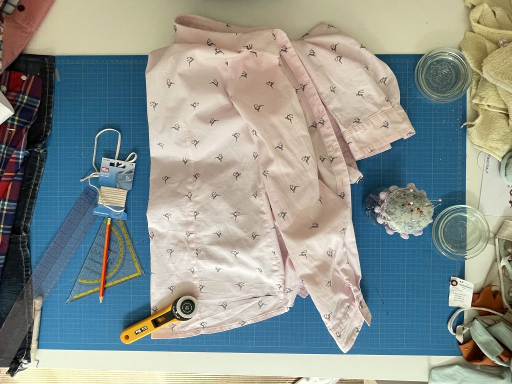 Eine rosafarbene Damenbluse mit kleine Hirschen darauf liegt auf einem Zuschneide Tisch zum Upcycling Bluse