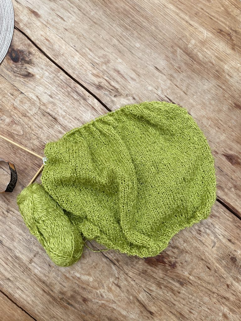 ein grünes Strickstück liegt auf einem Holztische. Es wird eine Stricktop