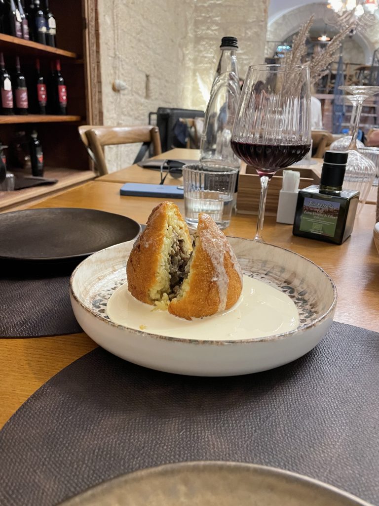 Arancina aufgeschnitten im Hinterrund ein Lokal auf Sizilien