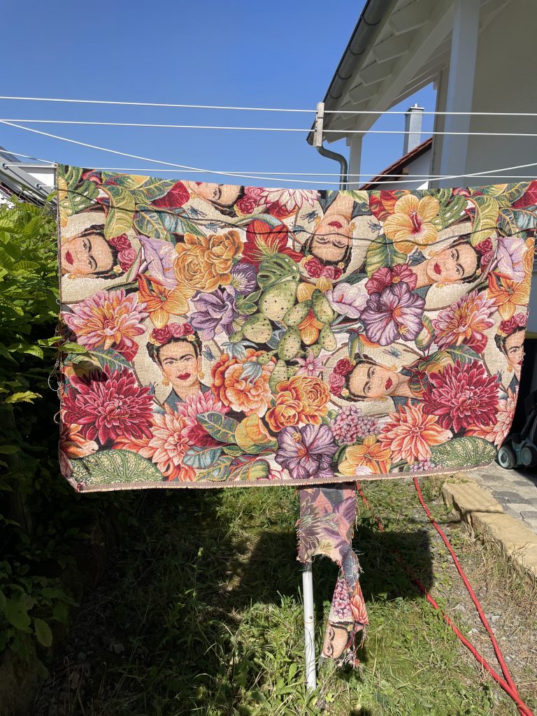 Ein Stoff mit Köpfen von Frida Kahlo und vielen Blumen hängt auf einer Wäscheleine