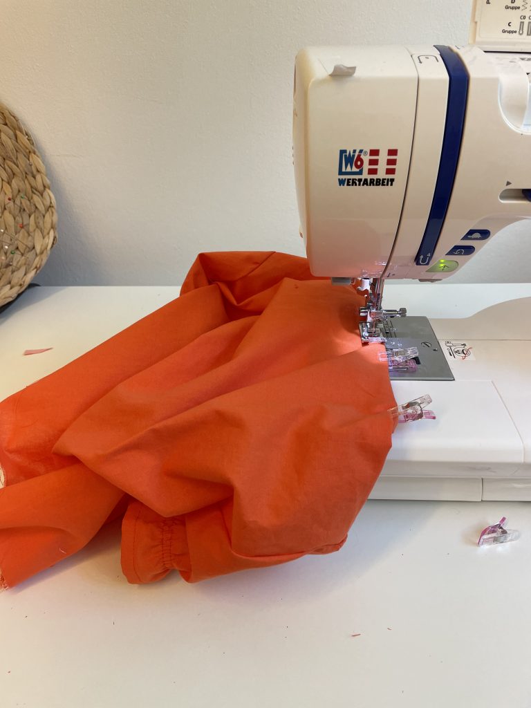 Ein Stoff der orangenen Dirndlbluse liegt auf der Nähmaschine