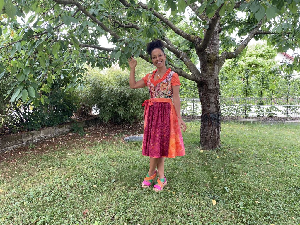 Eine lächelnde Frau in einem bunten Dirndl steht unter einem Baum