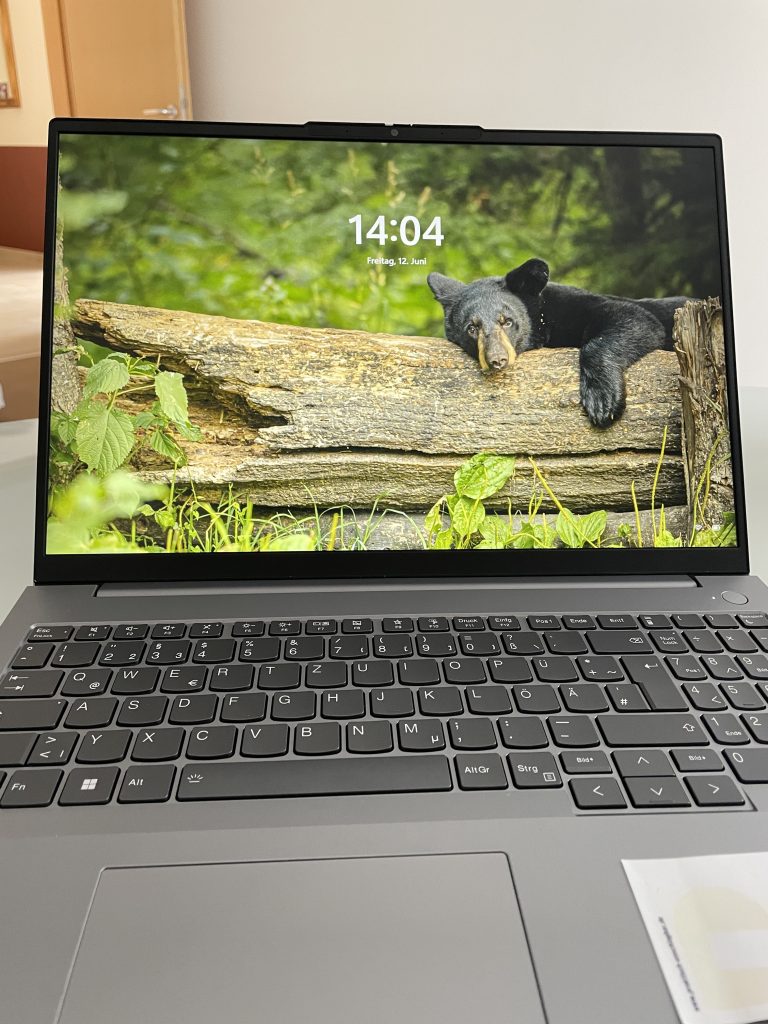 Ein geöffnetes Laptop mit einem Bild von einem Bär der auf einem Baumstamm ruht.
