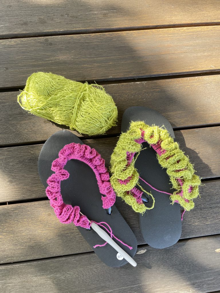 Flip-Flops. Der linke ist mit pinkfarbener Wolle umhäkelt, der rechte mit pink und oben drauf mit grüner wuscheliger Wolle.