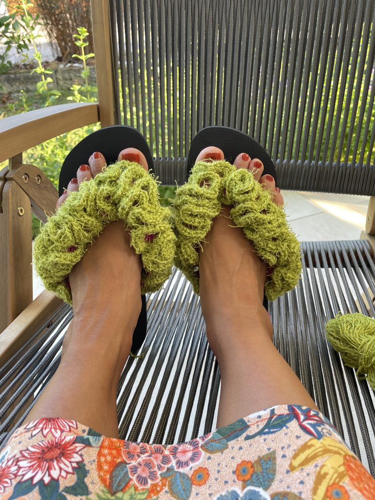 Flip-Flops umhäkelt an Füßen die auf einem Gartenstuhl liegen