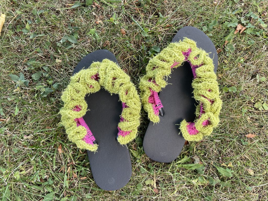 Flip-Flops umhäkelt stehen auf einer Wiese.