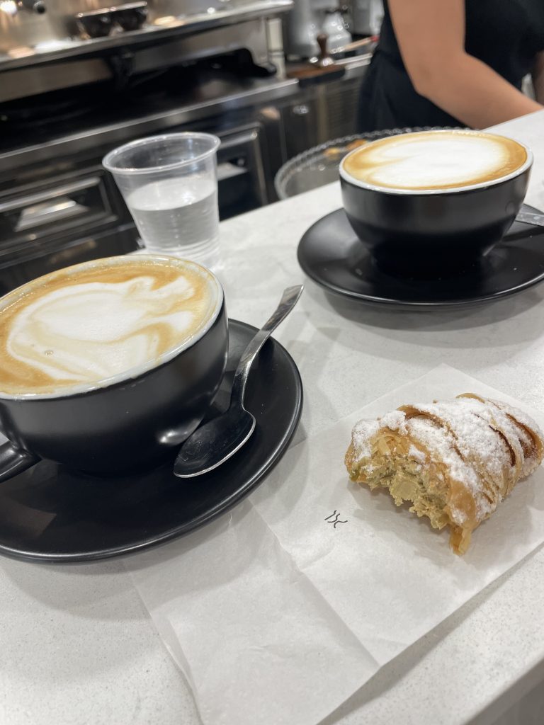 Zwei Cappuccino stehen auf dem Tresen einer Bar in Apulien, davor ein angebissenes Sfogliatelle" mit Pistaziencreme gefüllt