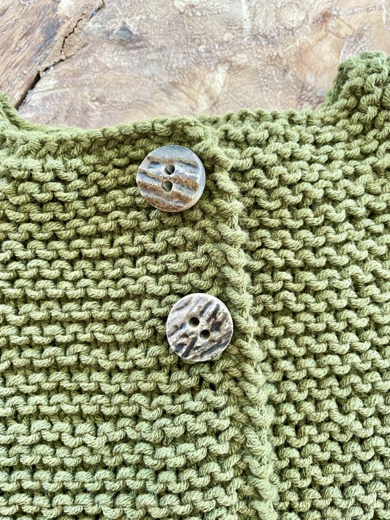 Eine Teil einer BabyStrickjacke mit 2 Knöpfen.