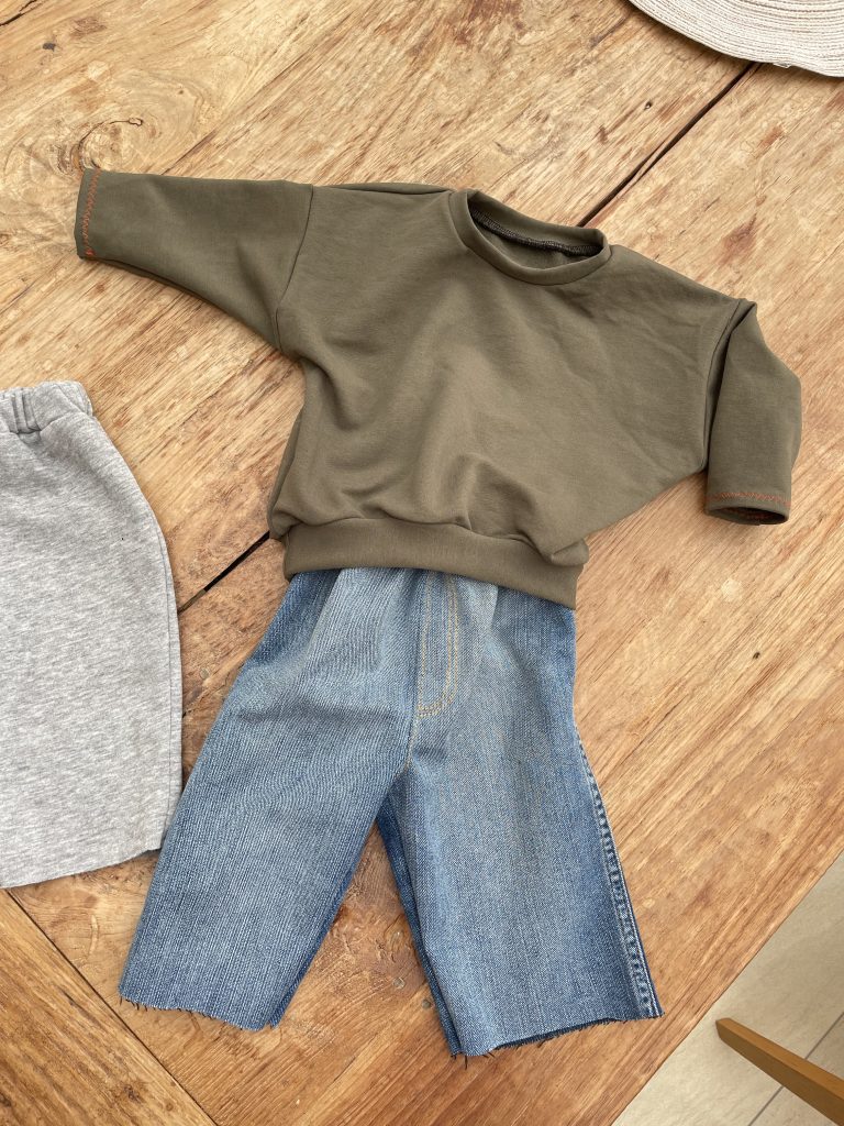 Ein Grüner Bybypullover, eine Babyjeans auf einem Holztisch