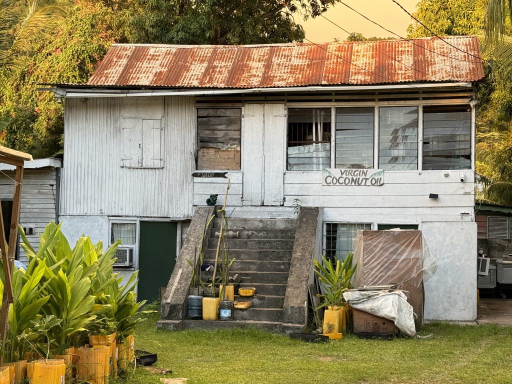 Ein altes Haus auf den Seychellen mit Brettern Wellblechfassade. Auf dem Schild an der Wand steht "Virgin Coconut Oil"