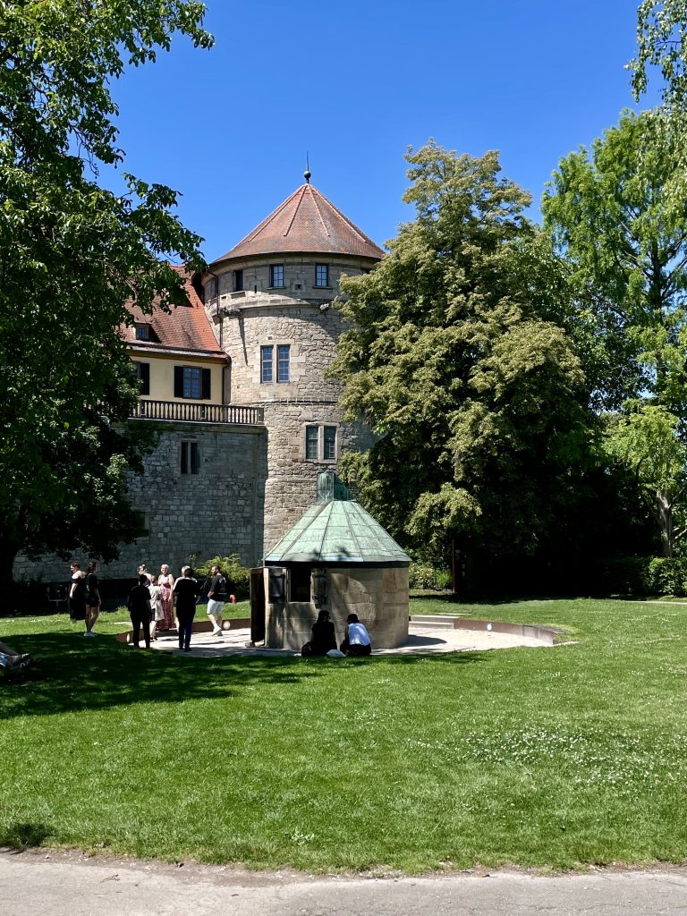 Historische Camera Obscura im Schlossgarten des Schlosses Hohentübingen in Tübingen an einem sonnigen Tag, umgeben von Besuchern und grüner Wiese. Das optische Instrument aus dem 19. Jahrhundert wurde zur Himmels- und Landschaftsbeobachtung genutzt und gehört heute zum Museum der Universität Tübingen.