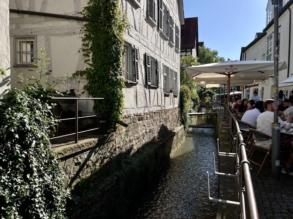 Romantischer Altstadtblick in Tübingen mit Fachwerkhäusern, schmalem Kanal und Straßencafé – beliebter Treffpunkt mit historischem Flair und typischer Neckaridylle im Sommer.