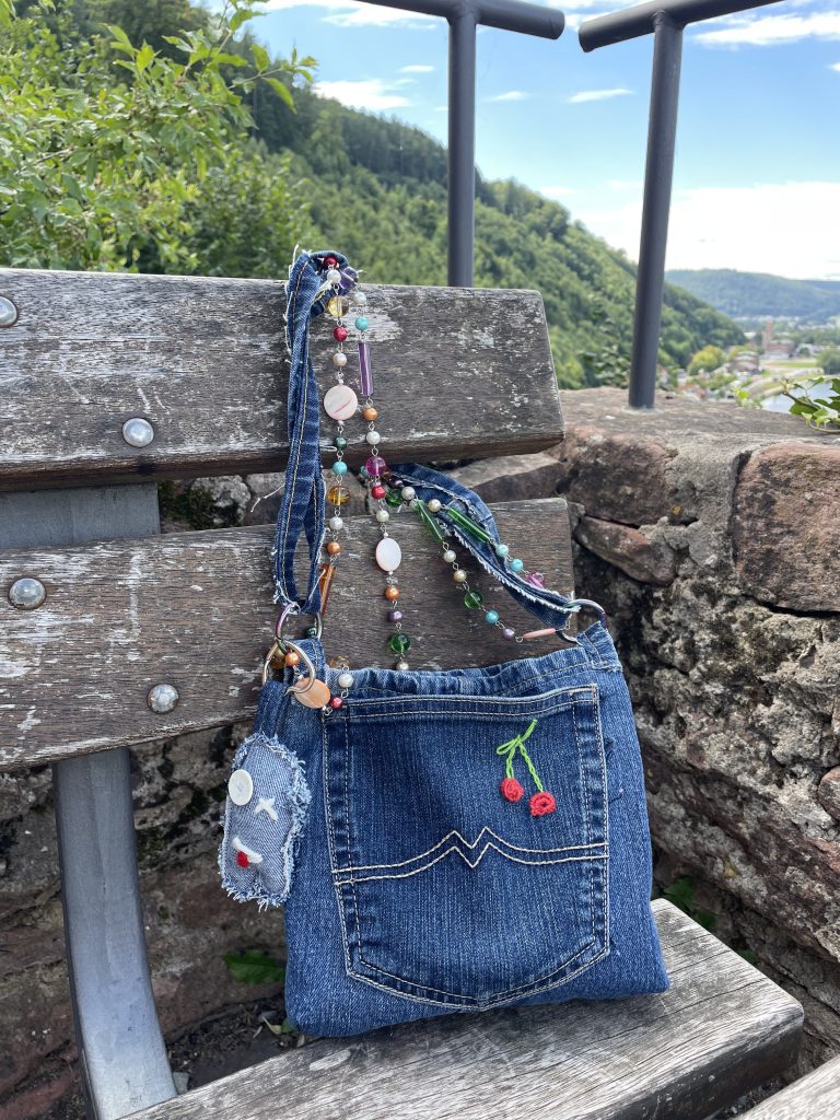 Jeanstasche steht auf einer Bank. Im Hintergrund ist Gebüsch