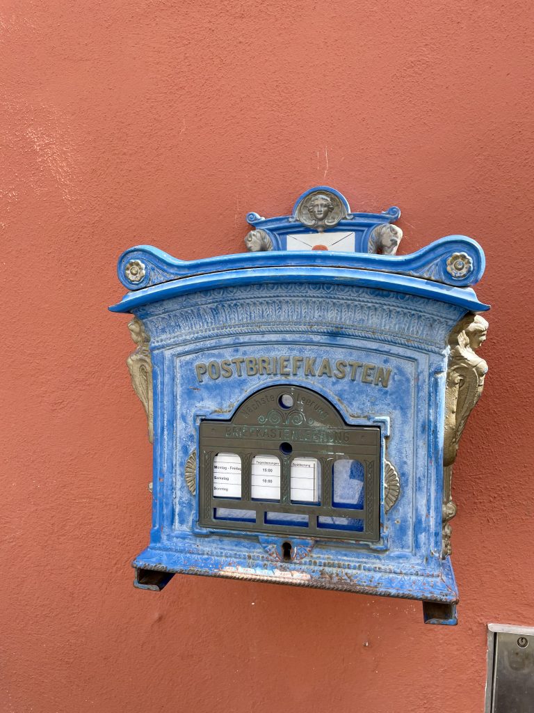 Ein blauer reich verzierter Postbriefkasten an einer terracottafarbenen Hausmauer