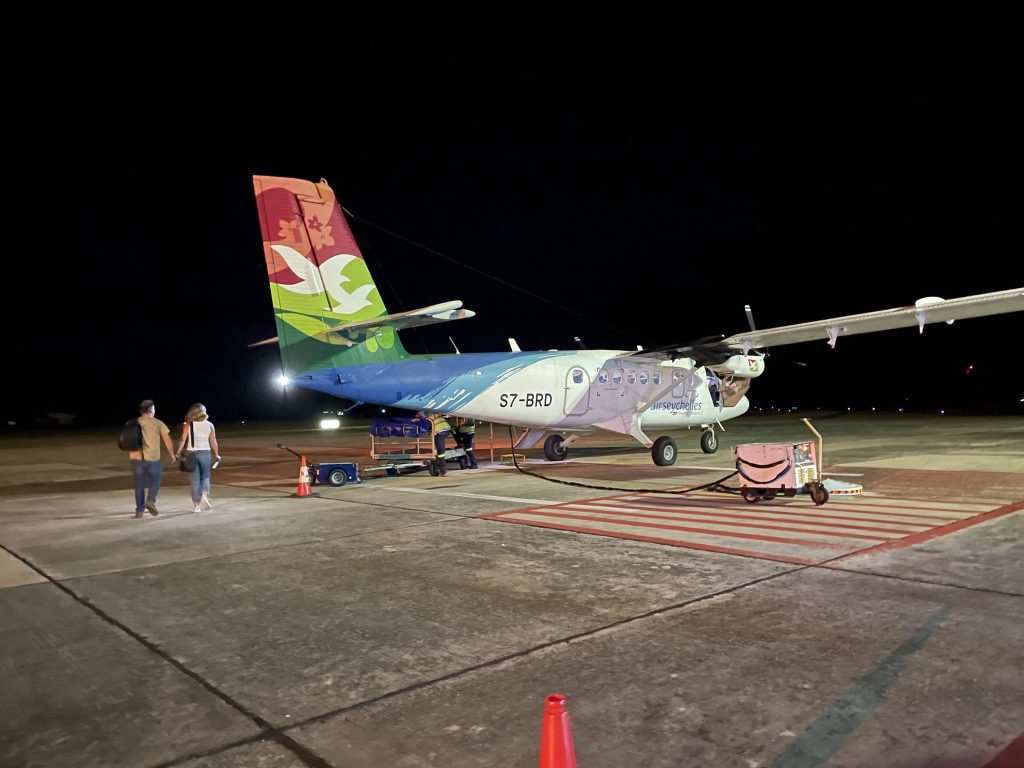 Ein buntes kleines Flugzeug steht auf dem Flugplatz. 2 Personen laufen auf es zu.