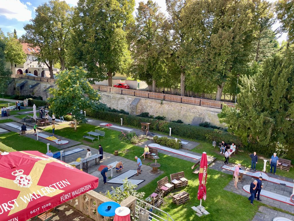 Minigolfplatz in Nördlingen hinter der Stadtmauer. Viele Menschen spielen an einem sonnigen Tag.