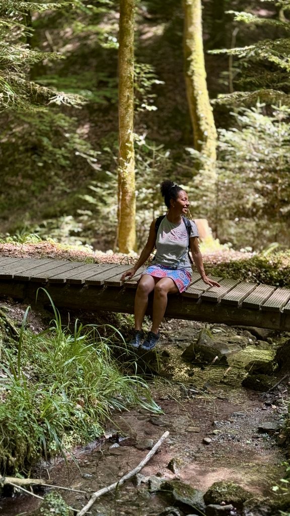 Eine Frau sitz auf einer Holzbrücke im Wald. unter ihr fließt einBach