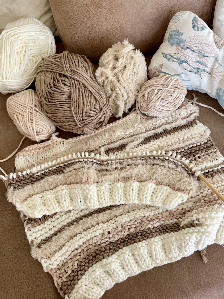 Einige Wolleknäul und unfertig gestrickte Teile eines Pullovers liegen auf einer lederartig aussehenden Fläche